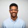 Profile picture of a smiling individual with glasses, wearing a light blue shirt against a neutral background.